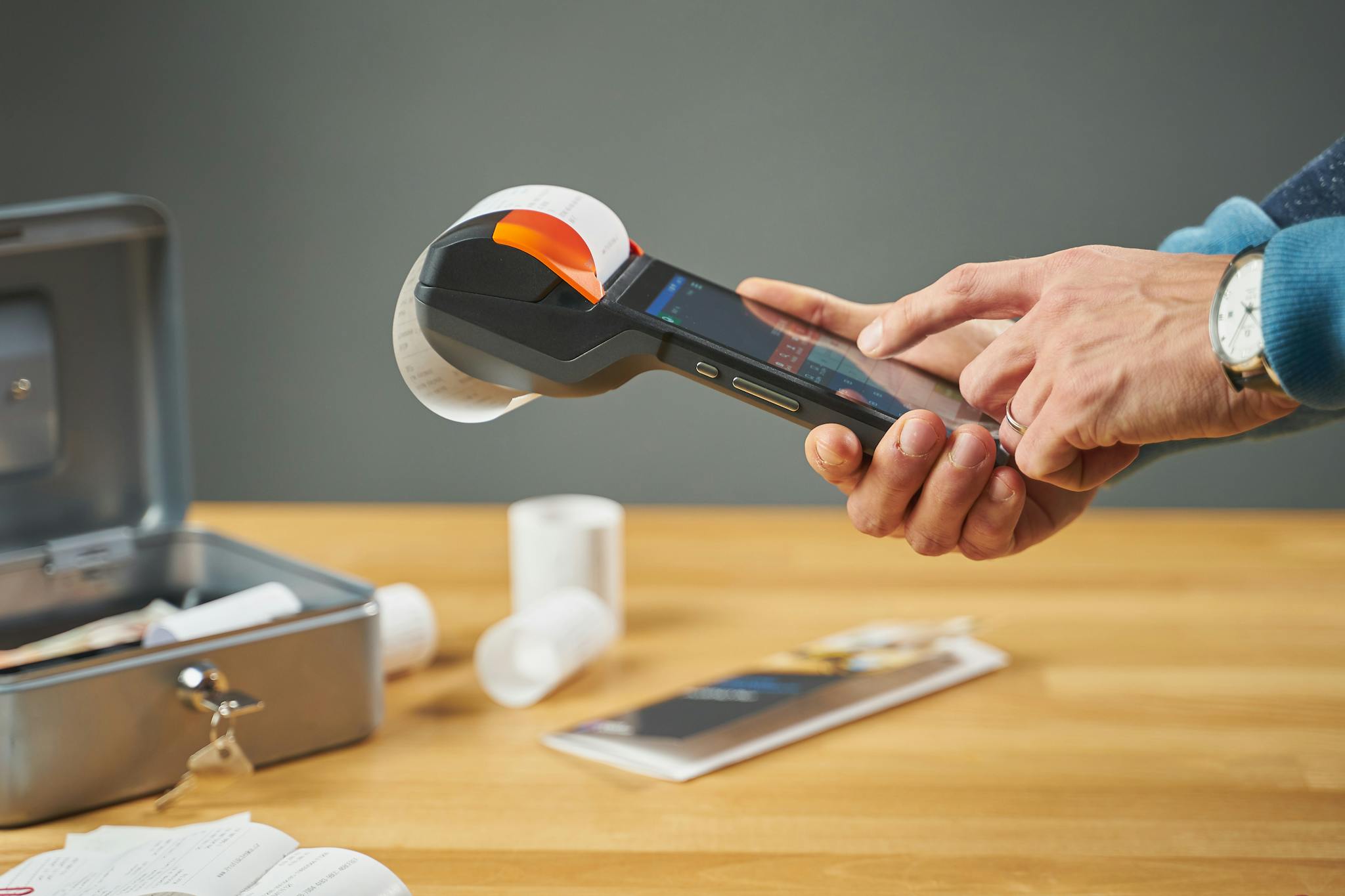 Hands operating a portable receipt printer with printed receipts on a wooden table.